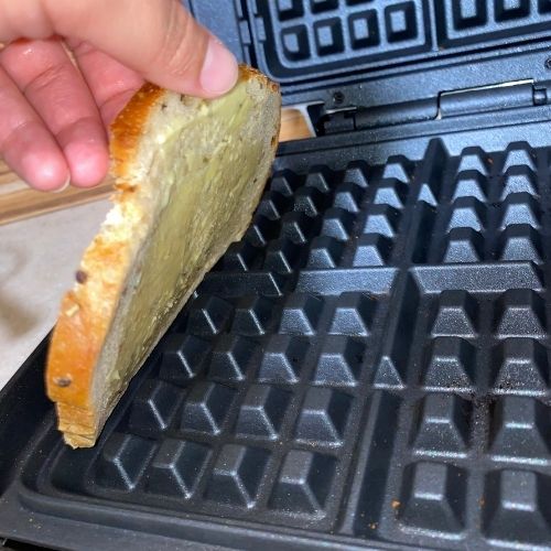 hand placing buttered bread on waffle iron