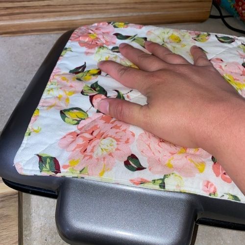 hand pressing down on waffle maker with a pot holder