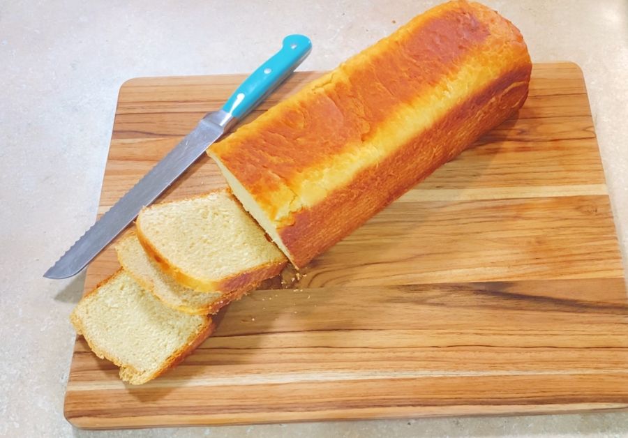 unsliced loaf of bread with 3 slices off on a cutting board with a blue bread knife
