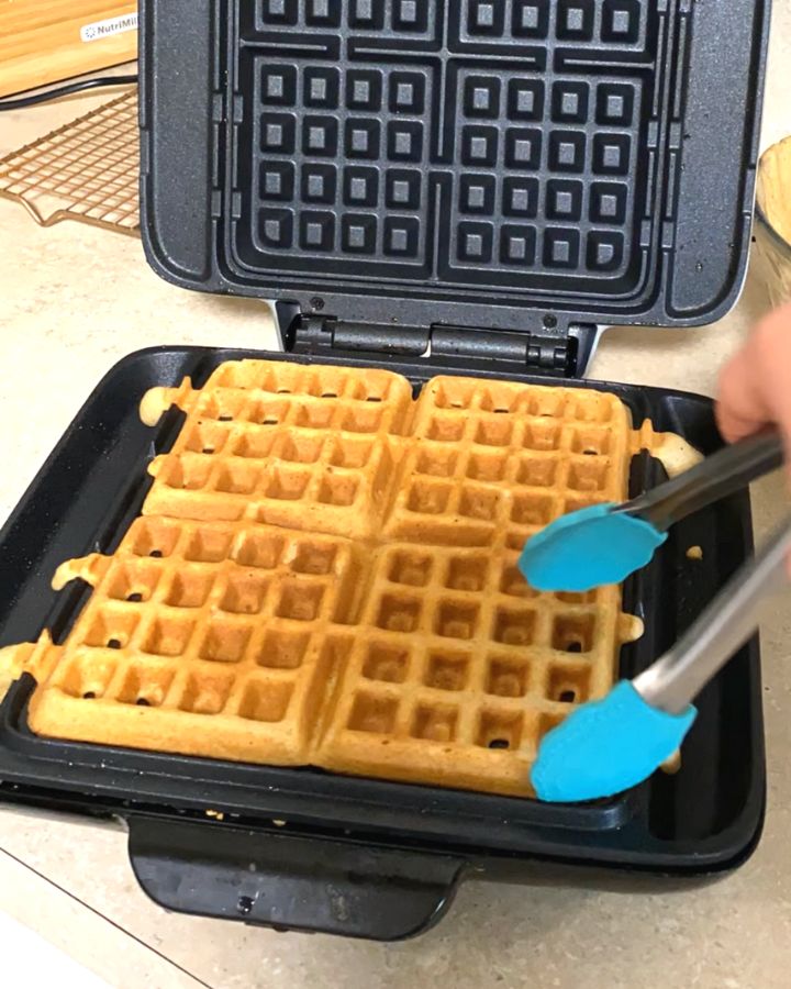 taking cooked waffle out of waffle iron with tongs.