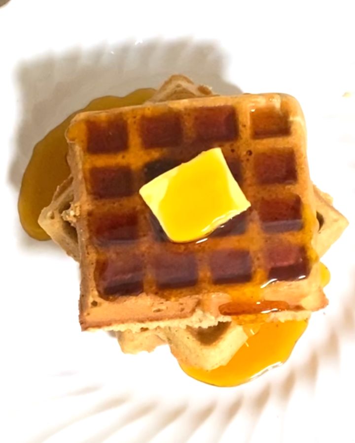 A stack of Ezekiel waffles with a pad of butter and maple syrup on top.