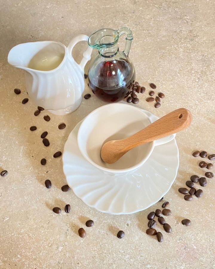 empty coffee cup with cream and maple syrup beside it and whole coffee beans scattered around.