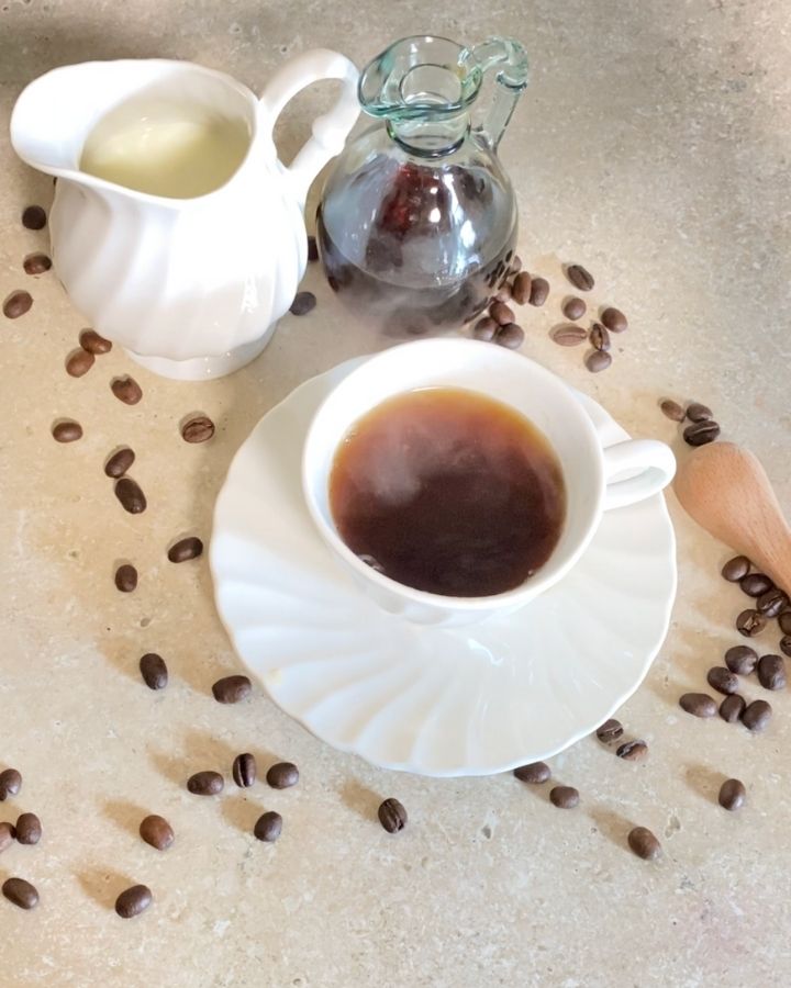 Steaming hot coffee in a cup on a plate with whole coffee beans scattered.